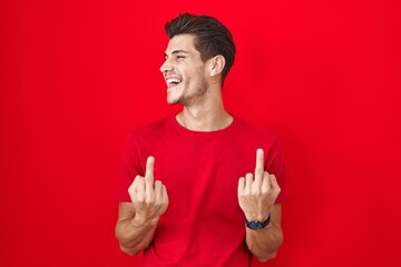 Young hispanic man standing over red background showing middle finger doing fuck you bad...