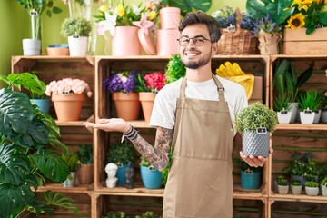 Young hispanic man with tattoos working at florist shop holding plant celebrating achievement with...