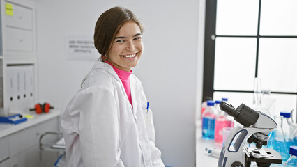 Radiant young hispanic woman, a confident scientist, joyfully smiling amidst her laboratory work, a beautiful expression of confidence in scientific research