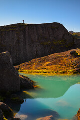 A hiker enjoys the view of the huge boulders and turquoise ponds of the Storurd hiking trail, East Fjords, Iceland.