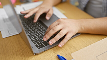 Close-up of a young adult's hands typing on a laptop, suggesting an office environment without showing the person's face.