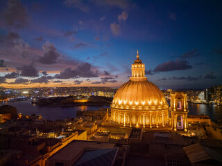 Aerial view of illuminated dome of Basilica of Our Lady of Mount Carmel in Valletta, Malta. View towards Manoel island with fort and Sliema skyline.