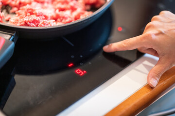 setting the right temperature on ceramic cooking top, mince meat in frying pan.