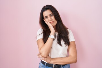 Young brunette woman standing over pink background thinking looking tired and bored with depression problems with crossed arms.