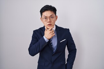 Young asian man wearing business suit and tie looking fascinated with disbelief, surprise and amazed expression with hands on chin