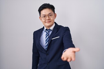 Young asian man wearing business suit and tie smiling cheerful offering palm hand giving assistance and acceptance.