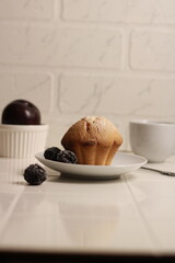 cupcake on a white saucer with berries and a cup on a white background