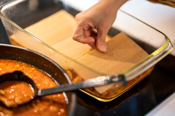 making lasagna, adding pasta to mince meat in ovenproof dish.