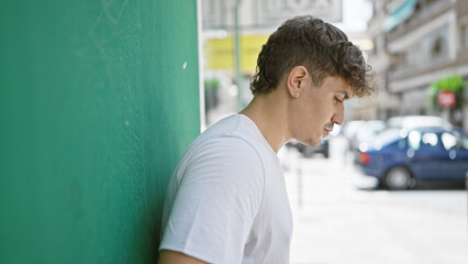 Cool, relaxed young hispanic man leaning on urban city wall, his handsome adult portrait shining...