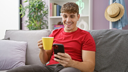 At home, a confident young hispanic man enjoys a morning cup of coffee, comfortably relaxed on the sofa. his handsome expression radiating positivity and joy from his infectious, heartwarming smile.