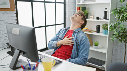 Overworked handsome young hispanic man working at office business table, hurt by sudden heart...