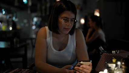 Young beautiful hispanic woman using smartphone sitting on the table at the restaurant