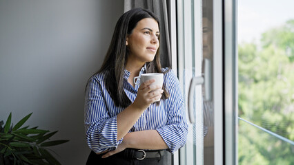 Young beautiful hispanic woman smiling looking through the window at home