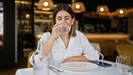 Young beautiful hispanic woman drinking a glass of water at the restaurant