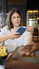 Young beautiful hispanic woman taking picture to food plate at the restaurant