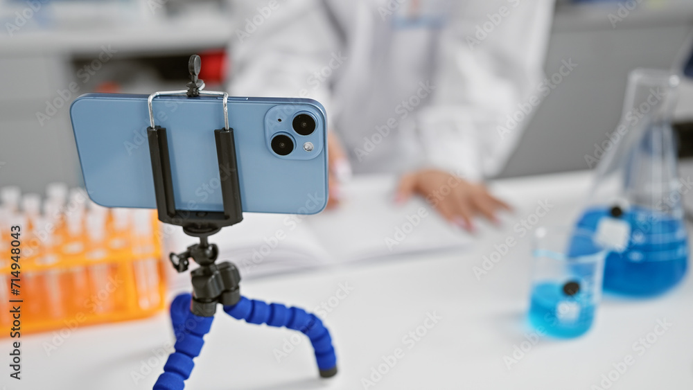 Poster Female scientist's hands busy taking notes while engaging in a video call conversation in her laboratory, an indoor medical research centre, wearing her work uniform