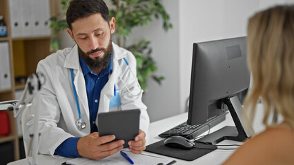 Young hispanic man doctor showing touchpad to patient at the clinic - obrazy, fototapety, plakaty