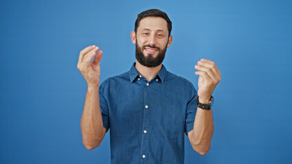 Fototapeta premium Young hispanic man smiling confident doing money gesture over isolated blue background