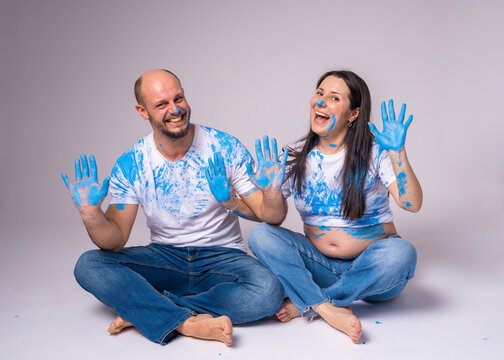 Happy couple at a gender reveal party. A man and a pregnant woman with a bare belly are painted blue and laugh very merrily.