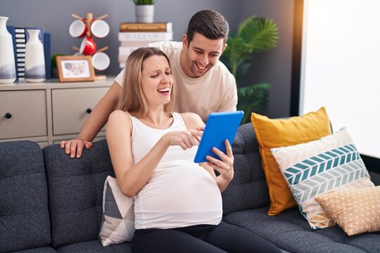 Man and woman couple using touchpad expecting baby at home