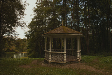 A gazebo in the middle of a yellow-green park, and a river flows below. The roof of the gazebo is...