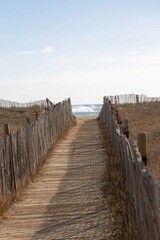 A wooden boardwalk flanked by fences leads through dunes towards the sea horizon