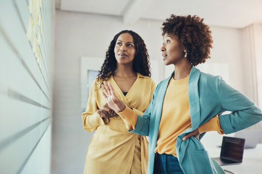 Businesswomen brainstorming using adhesive notes on an office wall