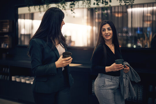 Smiling businesswomen talking over coffee while walking in a hotel lobby