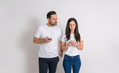 Fototapeta premium Suspicious man peeking into girlfriend's phone and trying to read her messages on white background