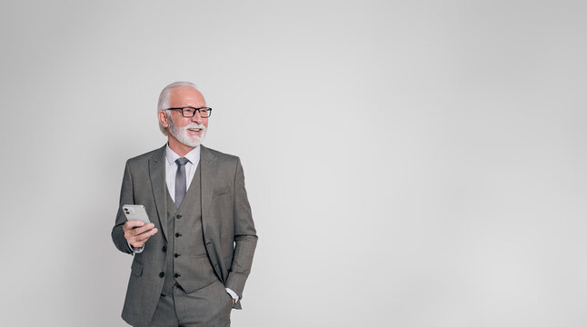 Happy senior businessman with hand in pocket and mobile phone looking away over white background