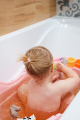Cute baby child bathes in pink bathtub with toys