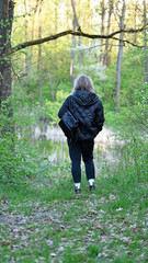 girl walking in the woods back view. young woman in spring forest. girl with a backpack, tourist. enjoying spring weather. Rest, relaxation, lifestyle concept, walk in the fresh air. hiking in nature