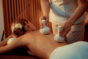 Obraz na płótnie Canvas Hot herbal ball spa massage body treatment, masseur gently compresses herb bag on woman body. Tranquil and serenity of aromatherapy recreation in warm lighting of candles at spa salon. Quiescent