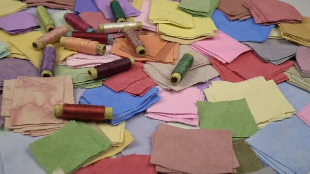 Spools of colored sewing threads fall on multicolored fabrics of homemade dyeing for patchwork, slow motion