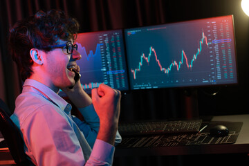 Successful business trader calling to broker, raising fist up with highest profit on global market online in real time at neon light modern office. Concept of stock exchange young businessman. Gusher.