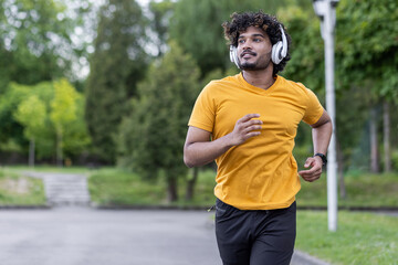 Indian young man doing sports and training in the morning, wearing headphones running in the park