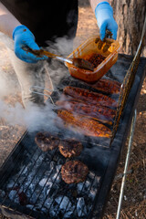 Glazing mackerel fillets with a basting brush on a smoky grill, surrounded by forest foliage