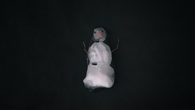 Snowman melts on black background. Overhead view of a real snowman melting quickly. Timelapse 4k video.
