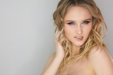 Fototapeta premium Young beautiful woman with blonde curly hair on grey background