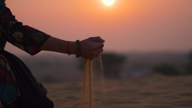 Woman's Hand Pouring Desert Sand against sunset sky at Thar desert in Jaisalmer, Rajasthan, India. Female pouring sand in the desert. 