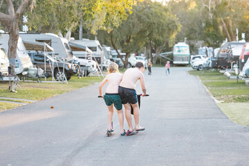 Kids riding scooters through caravan park on tropical holiday - obrazy, fototapety, plakaty