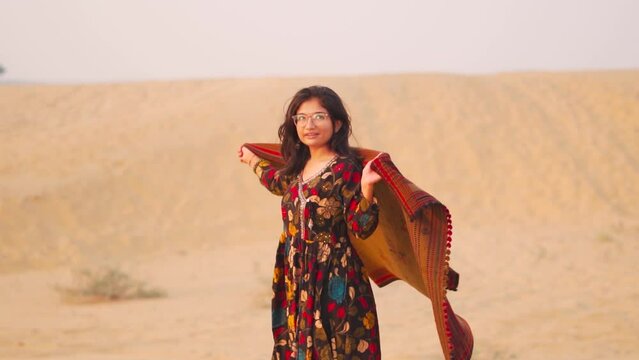 Portrait of young Indian woman wearing shawl while standing at Thar desert in Jaisalmer, Rajasthan, India.  Tourist enjoying Holiday. Desert Travel background.