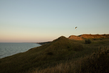 A seascape with a paraglider flying over the shore. Paragliding over the sea hills. A paraglider in the rays of the setting sun.