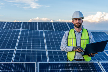portrait of an engineer smiling with confidence using a laptop in front of a solar panel power...