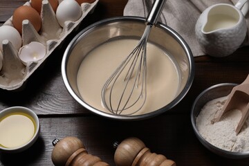 Fototapeta na wymiar Dough, metal whisk in bowl and ingredients on wooden table