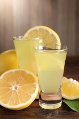 Tasty limoncello liqueur, lemons and green leaf on wooden table, closeup