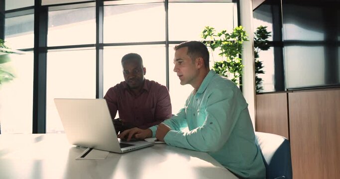 European and African male colleagues working on joint on-line task met in office boardroom look at laptop screen, discuss software. Mentor help with program to new employee, share skills. Mentorship