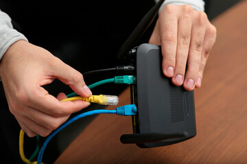 Man inserting cable into Wi-Fi router at wooden table indoors, closeup