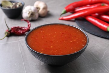 Spicy chili sauce in bowl on grey table
