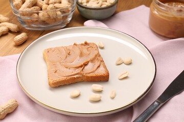 Toast with tasty nut butter, peanuts and knife on table, closeup